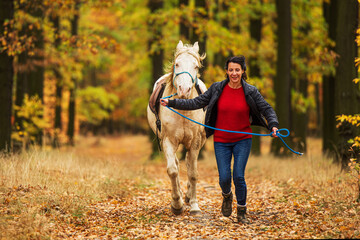 A pretty young woman and a white horse running through the woods side by side