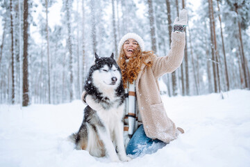 Cute woman playing with her dog in the snow. A happy woman and a Siberian husky are walking together in a snowy forest. The concept of holiday, relaxation.