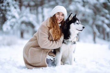 Cute woman playing with her dog in the snow. A happy woman and a Siberian husky are walking...