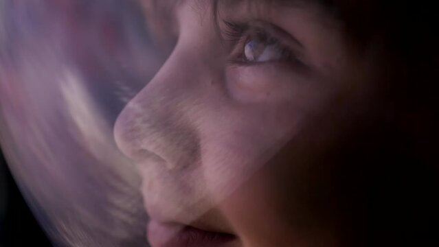 Portrait of a cute boy with big eyes happily looking at planet earth wearing a spacesuit helmet and looking through the glass from outer space. A teenager studies space. Spaceship simulator