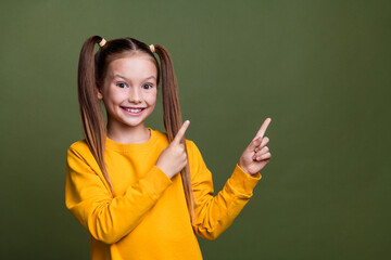 Photo of positive schoolgirl with ponytails wear yellow pullover indicating at sale empty space isolated on khaki color background