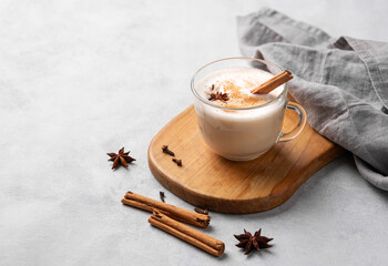 Traditional Indian masala chai latte in a glass cup. Hot drink with milk, spices and herbs on a wooden board on a light background. - obrazy, fototapety, plakaty