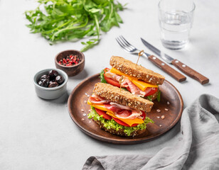 Two toast club sandwiches made of grain bread with cheddar cheese and bacon stuffed with tomatoes and lettuce and ruccola on a wooden plate on a light background.