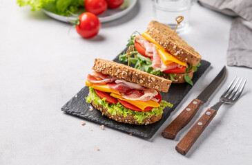 Two toast club sandwiches made of grain bread with cheddar cheese and bacon stuffed with tomatoes and lettuce and ruccola on a black board on a light background - Powered by Adobe