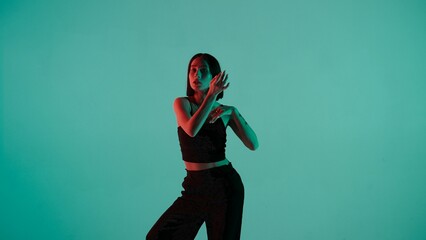 In the frame on a blue, light background. Dances young, beautiful girl. Demonstrates dance moves in the style of hip hop. Shes staring at the camera. Shes feminine in a black top and pants