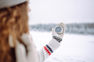 Close-up of a young woman in a hat holding a compass lying in her hand on a mitten against the...