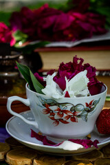 Garden composition, peony petals in a white cup, strawberries and books in the garden