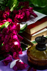 Vertical colorful garden composition, peony petals, oil lamp and books in the garden with selective focus on a sunny day.