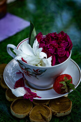 Garden composition, peony petals in a white cup, strawberries in the garden