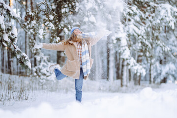 Fototapeta na wymiar Happy woman wearing scarf and hat on snowy winter day outdoors. Young woman having fun with snow on a frosty day. Walking concept.
