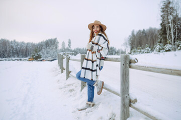 Happy woman in a hat and scarf walks near a winter lake in the winter forest. Winter walk concept. A young tourist woman enjoys a frosty day outdoors.