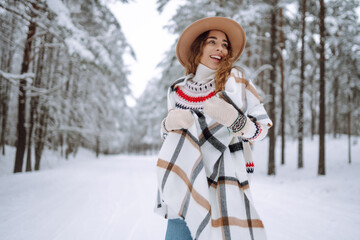 Beautiful woman in fashionable winter clothes outdoors. A woman walks in a hat and scarf in a winter snowy forest. Lifestyle.