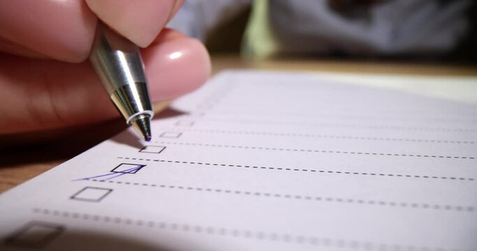 Closeup of hand putting checkmark or marking with blue pen on checklist and checkbox and to-do list