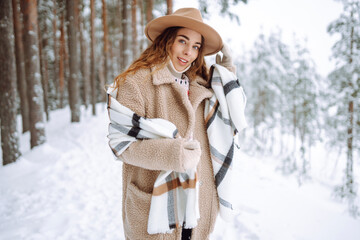 Fototapeta na wymiar Winter walk. A young woman in winter clothes is having fun in a snowy forest. A beautiful female tourist in a hat enjoys a frosty day in the forest.