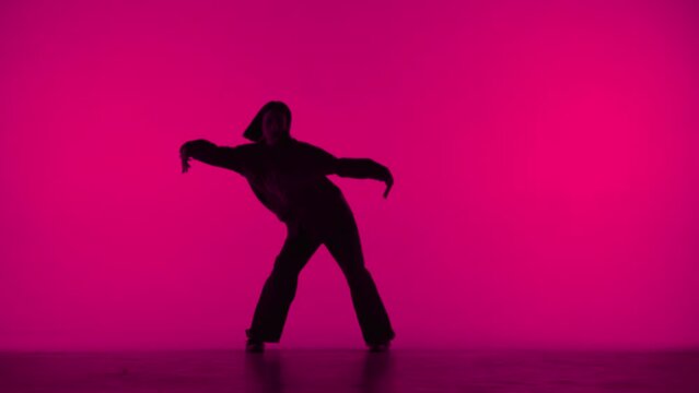 In the frame on the pink background in the silhouette. Dances slender, beautiful girl. Demonstrates dance moves in the style of hip hop. It is feminine, plastic, rhythmic