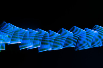Fototapeta premium Blue neon wave of light as curls or swirl with smooth stripes on black background. Abstract background with dynamic line in motion, light painting in modern style.
