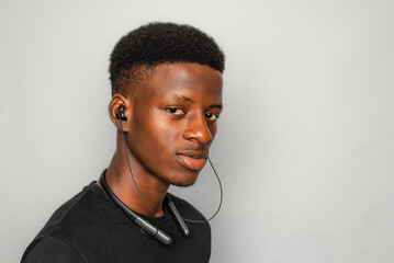 Male Gen Z portrait against white backdrop puts some expression on face with a wireless ear piece on his neck with a bold confident look