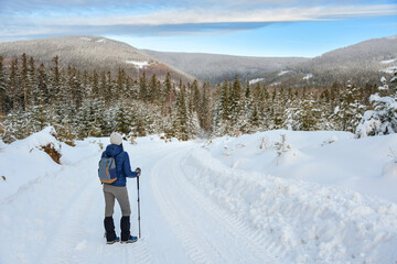 A young woman is standing on a snow-covered hiking trail and admiring the panorama of the Sudetes mountains.