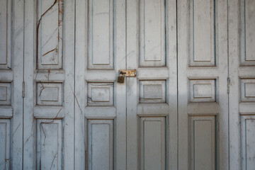 Old wooden white dirty folding door is closed and locked by master key.