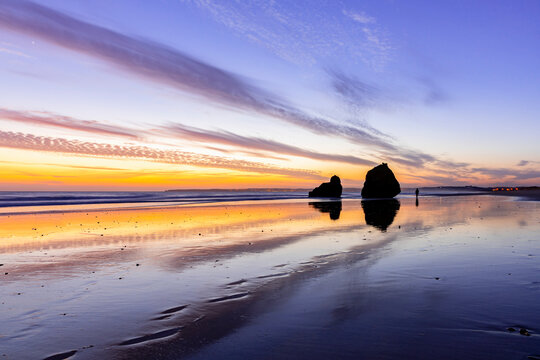 Twilight Tapestry: Praia dos Tres Irmaos Beach, Alvor, Portugal, where Vibrant Sunset Colors Paint the Sky, Reflecting in the Tranquil Waters, with Coastal Rocksand a Lone Walker