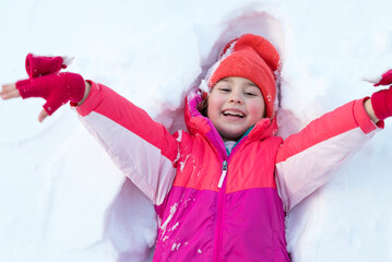 Top view portrait of happy kid  lying in snow in winter nature
