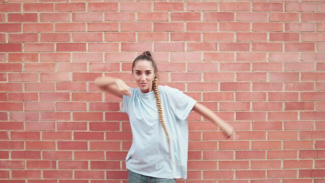 Young woman dancing popping against a brick wall in the city street. Active dancer performing hip hop with robotic moves in the street. Freestyle dancer. 