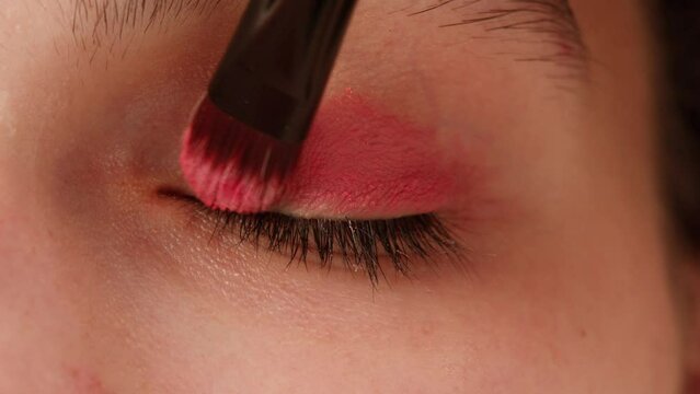 Eye shadow makeup to the upper eyelid, close-up. Makeup artist applies a bright eye shadow with a makeup brush.Tutorial master class of professional makeup. 
