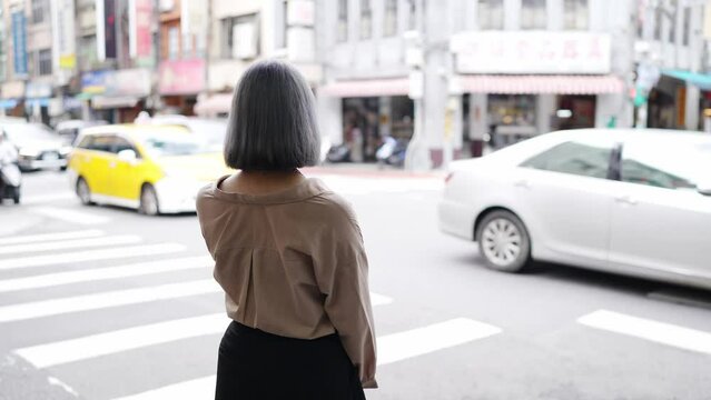 台北の伝統的な町並みである迪化街で交差点で立っている若い台湾人女性 A young Taiwanese woman standing at an intersection on Dihua Street, a traditional Taipei neighborhood.