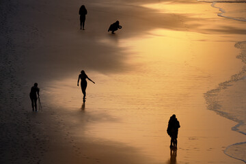 Menschen am Sandstrand im goldenen Licht des Sonnenuntergangs, fotografieren oder genießen ihren...