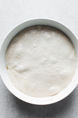 Focaccia dough in a white bowl, process of making focaccia, dough rising in a white mixing bowl	