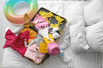 Open suitcase with beach accessories on bed in room