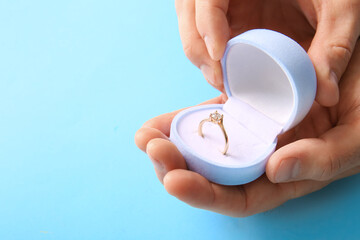 Man holding box with engagement ring on blue background, closeup
