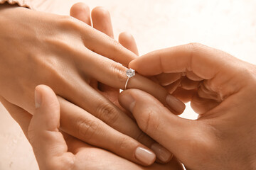 Man putting engagement ring on woman's finger against white background, closeup