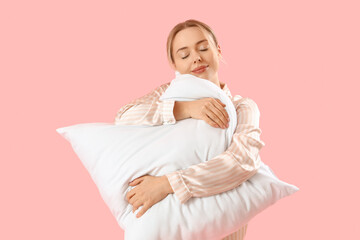 Young woman in pajamas with pillow on pink background