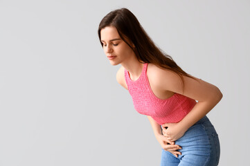 Young woman having menstrual cramps on light background