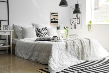 Cozy bed with white blanket and pillows in interior of stylish bedroom