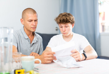 Son and his father sitting at the table and perusing letter.