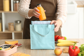 Mother packing bottle of juice into lunch box bag on table in kitchen