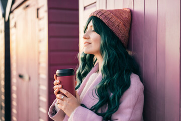 Stylish young smiling hipster woman with closed eyes wearing color hair, pink coat, hat holding...