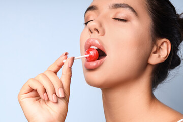 Young woman with beautiful lips eating lollipop on blue background, closeup