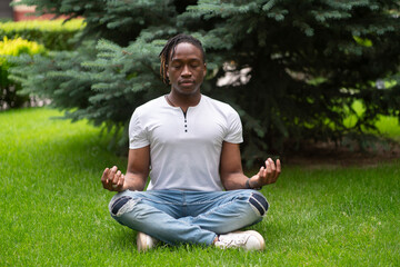 a stylish man meditating and doing yoga on the grass in the park