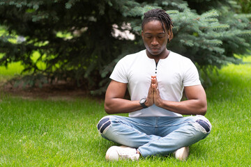 Naklejka na ściany i meble a stylish man meditating and doing yoga on the grass in the park