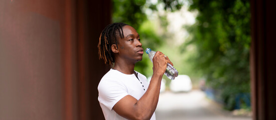 a athletic black man jogging in the streets. feel thirsty and drinking water from bottle