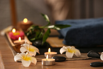 Obraz na płótnie Canvas Burning candles with plumeria flowers on table in dark spa salon, closeup