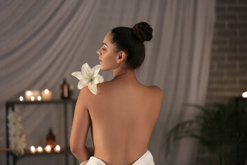 Beautiful young woman with flower relaxing in dark spa salon, back view