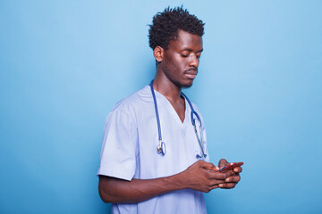 Portrait of African American medical professional stands against blue background holding modern...