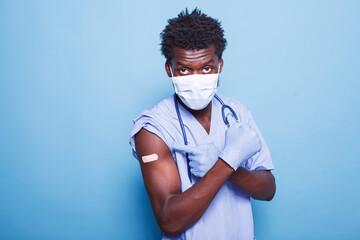 African American nurse directing attention to vaccine injection site with a bandage while making...