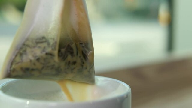 tea with milk, bag of herbal green tea is lifted from a white cup, a delicious drink flows onto the table, milk foam, whipped cream close-up, benefits for colds, warm up, drink a hot medicinal elixir