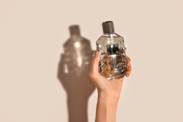 Female hand with bottle of luxury perfume on beige background