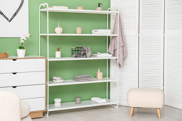 Obraz na płótnie Canvas Modern shelf unit with pouf and folding screen near green wall